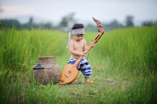 Asian fishing boy playing a wooden mandolin in the green rice field at the county side of 