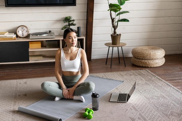 Asian fitness girl doing workout at home with laptop guide sport application on computer sitting on ...