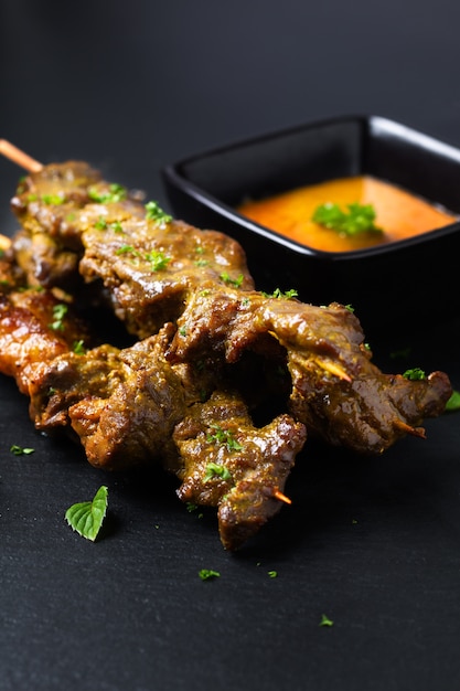 Asian food concept  homemade beef satay grilled and spicy peanut spice sauce  on black slate board with copy space