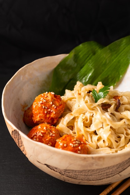 Asian Food concept homemade oriental egg noodles and spicy meatballs in ceramic bowl on black background