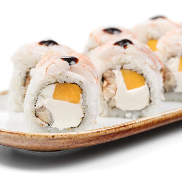 Фото Азиатская еда суши roll kyoto с рисом, сливочным сыром, нори, угри, манго, креветками, соусом, унага на белом фоне