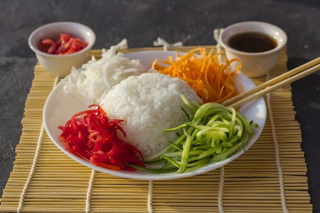アジア料理：暗いクローズアップに白いご飯と野菜（ニンジン、キュウリ、大根）。