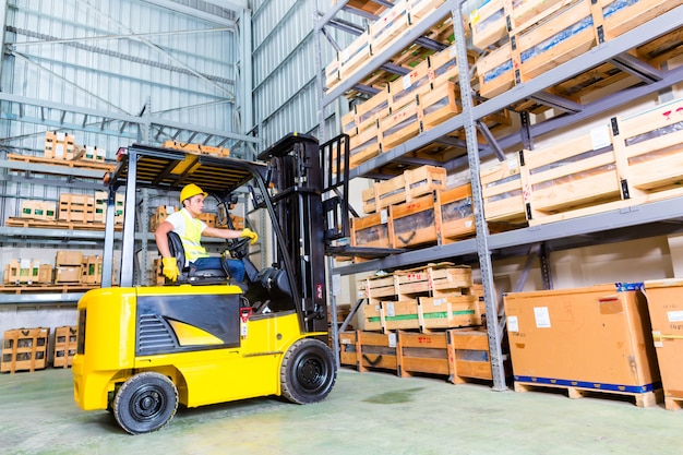 Asian fork lift truck driver lifting pallet in storage