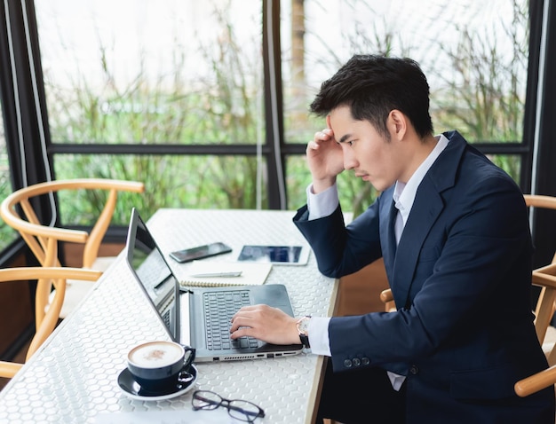 Asian freelance man wear suit and hand over head having stressful depression sad time while working on laptop at home Depression man sad serios working from home Working at anywhere concept