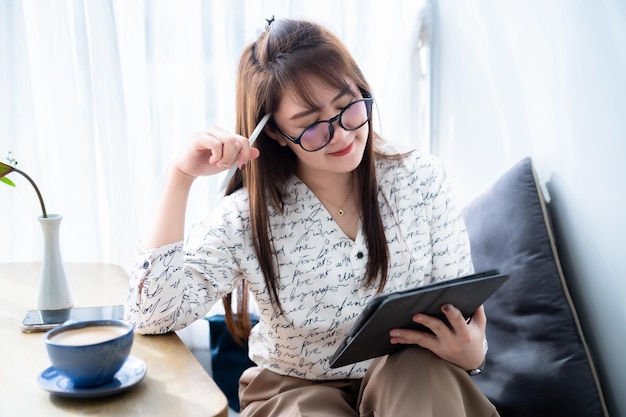 Asian freelance people business female thinking on something casual working with Draw or taking note on tablet with electronic pen for browsing internet chatting and blogging with coffee cup in shop