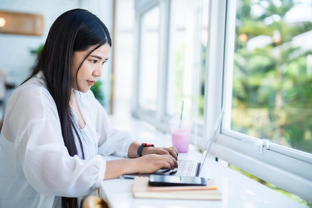 Asian freelance people business female wearing smartwatch talking making using casual working with laptop computer for browsing internet chatting and blogging and smartphonenotebook in coffee shop