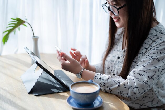 사진 아시아 프리랜서 비즈니스 여성 스마트폰으로 메시지를 쓰고 디지털 태블릿에서 메모를 작성하고 전자 펜으로 인터넷을 탐색하고 커피 컵으로 채팅하고 블로그를 작성합니다.