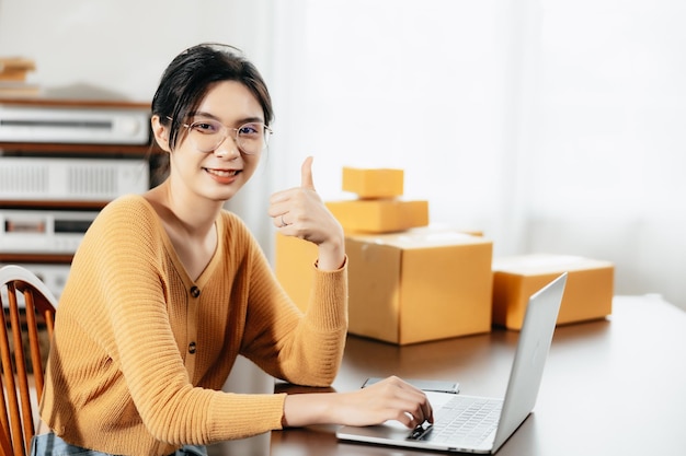 Donna asiatica freelance che utilizza il computer portatile per controllare le scatole di spedizione online degli ordini dei clienti a casa