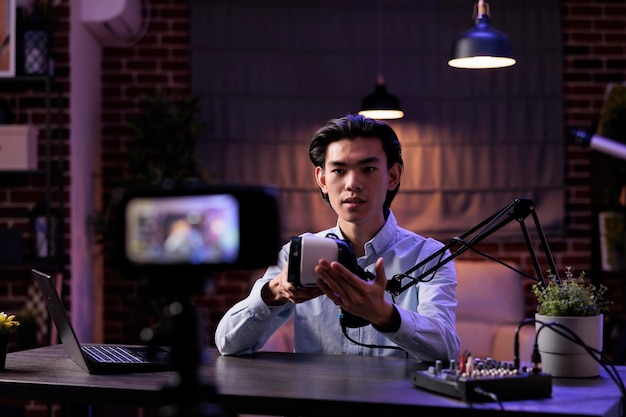 Asian freelancer filming product review with vr glasses, broadcasting live podcast on camera. Recording virtual reality goggles recommendation on livesteam, creating social media channel content.