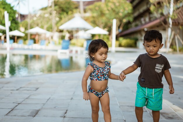 アジアの楽しい幼児は手をつないで外で遊ぶのを楽しむ