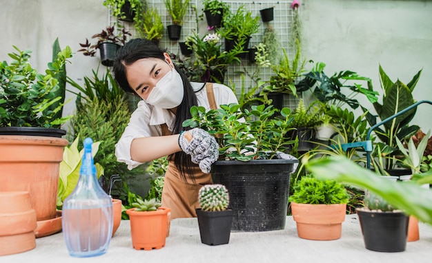 Foto donna asiatica del giardiniere che indossa maschera facciale e grembiule che usa la pala per trapiantare piante d'appartamento e cactus