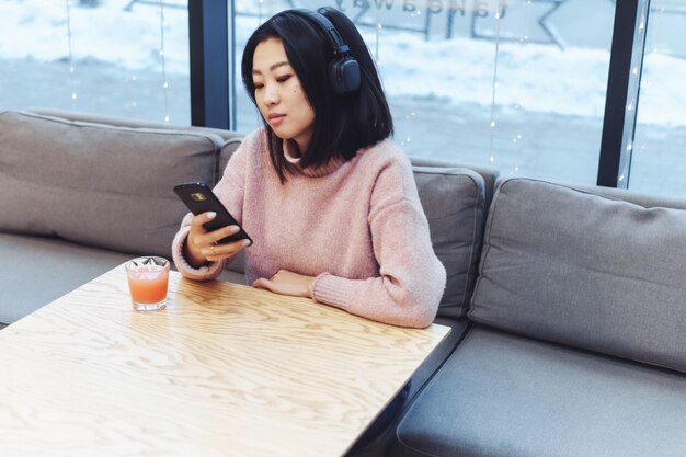 Asian girl alone in the city sits in a cafe and listens to music. Enjoying music in a public place