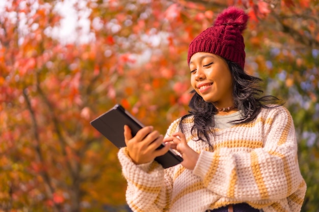 紅葉の森で手にタブレットを持つ秋のアジアの女の子は、技術コンセプトを残しています