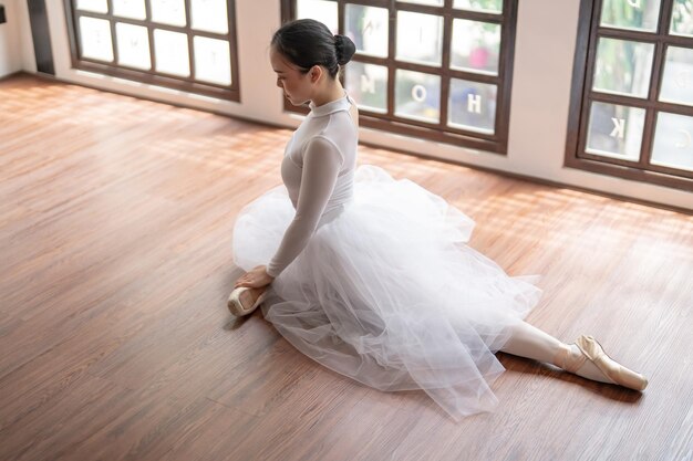 Asian girl ballet dancer gymnastic exercises in studio for body flexibility Ballerina training stretches her leg and prepares for performance practice routine