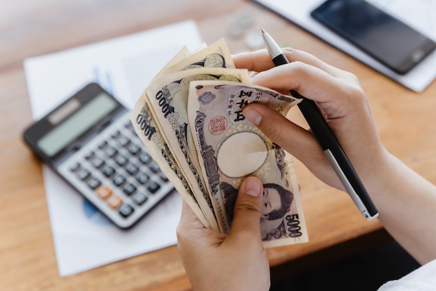 Ragazza asiatica che conta il calcolatore di yen giapponesi per contabilità personale