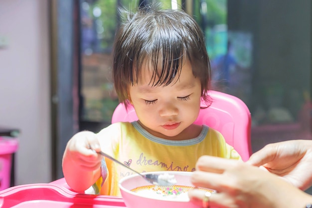 Photo asian girl eating fried sausages in the aluminium bowl near window at home