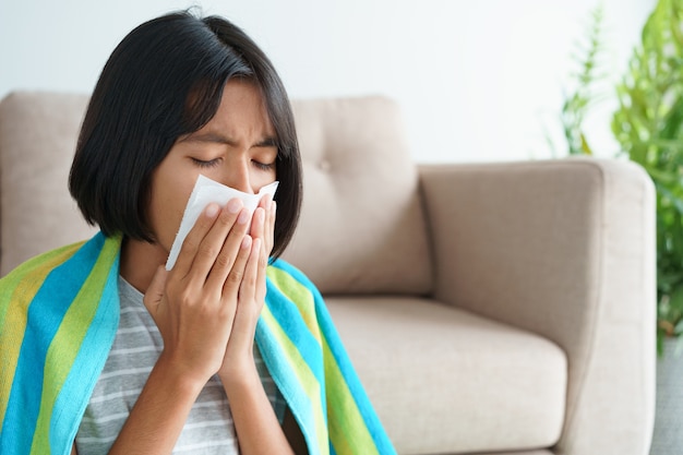 Фото Азиатская девушка, у которой сезон гриппа, чихает, используя бумажные салфетки, сидя в гостиной дома.