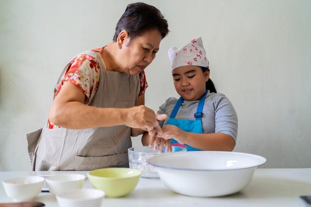 An Asian girl and her grandmother are helping each other make sweets She is learning cooking secrets from her grandmother