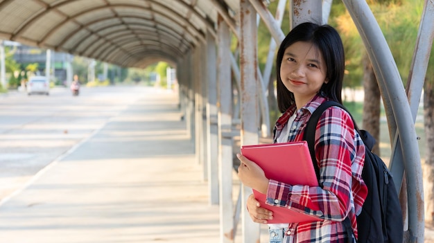 Asian girl hold book and backpack at school