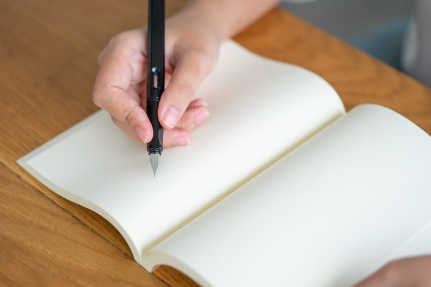 Asian girl holding a black pen writing into an empty book.