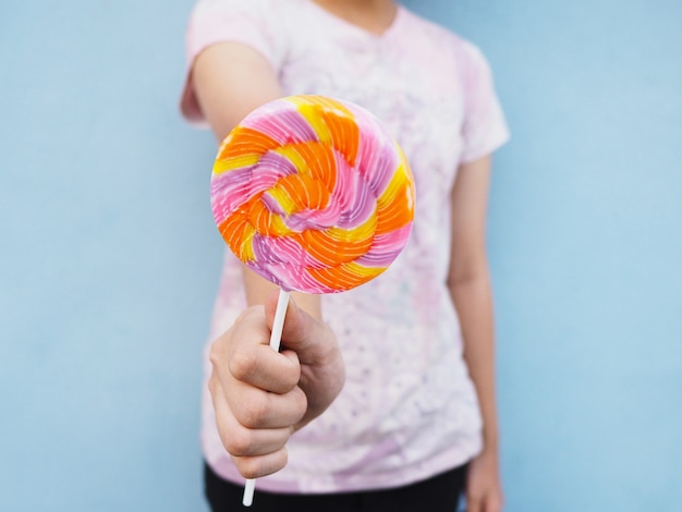 Asian girl holding colorful lollipop on hand and giving to friend over blue wall.