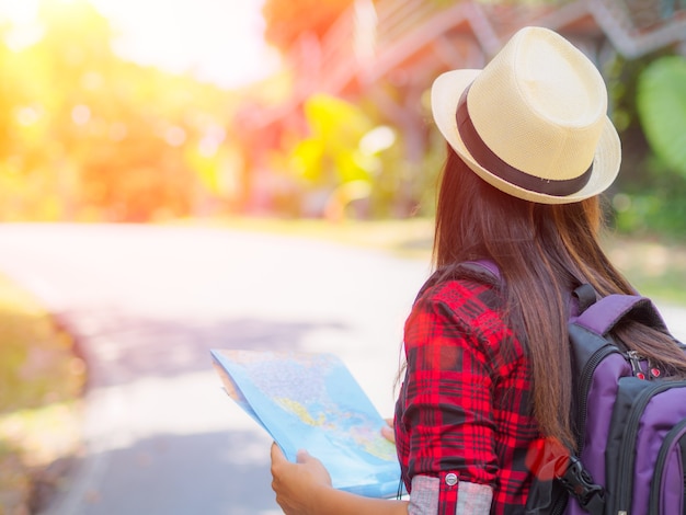 道路と森林のバックパックで地図を保持しているアジアの女の子の背景。