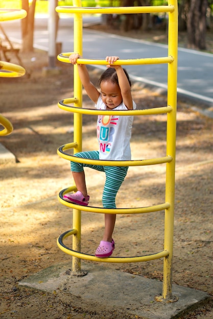 An Asian girl is climbing on a playground equipment in a school.