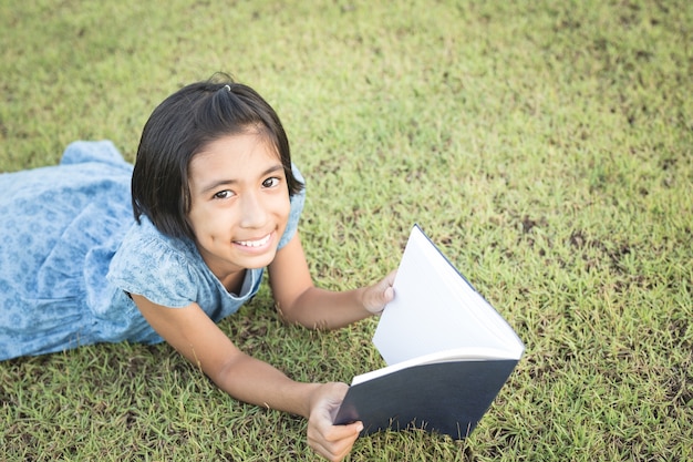 アジアの女の子が庭の本を読んでいます。