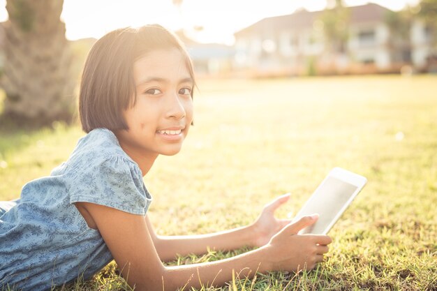 アジアの女の子は庭にタブレットを使用しています。