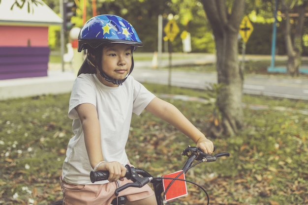 アジアの女の子は公園で自転車に乗ることを学びます。自転車に乗ってかわいい子供の肖像画。