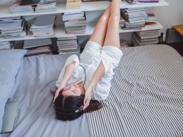 Asian girl listening music in headphones on bed