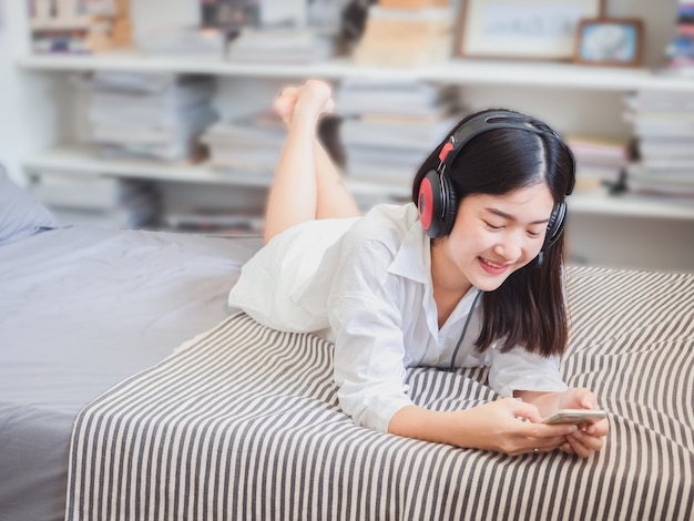 Asian girl listening music in headphones on bed