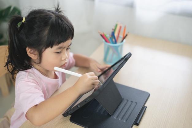 Asian girl looking and touch on white screen at the tablet screen attentively overstimulated children concept Too much screen time Cute girl watching videos while tv is working