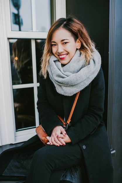La ragazza asiatica guarda in cappotti sui sorrisi della via