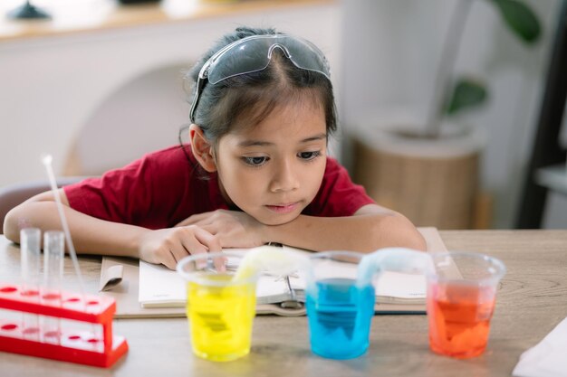 Asian girl making Walking Water experiment Food color is added to the water in the glass water moves along the paper and then color is mixed Concept of science for kid