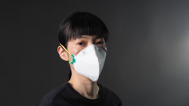 Asian girl in a mask on a black background in Coronavirus Quarantine situation Title about