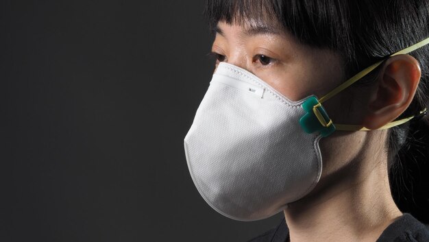 Ragazza asiatica in maschera su sfondo nero in situazione di quarantena di coronavirus