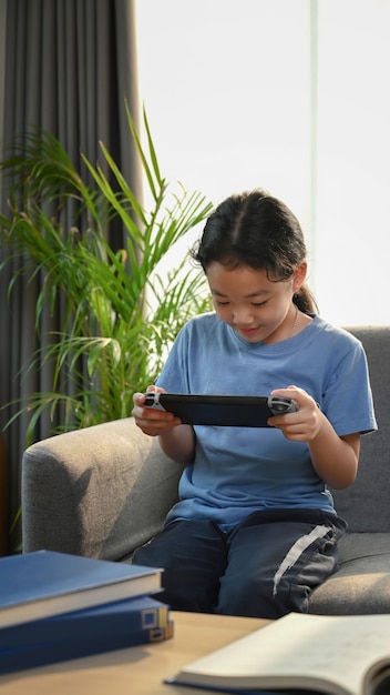 Asian girl playing games and sitting on sofa in living room.