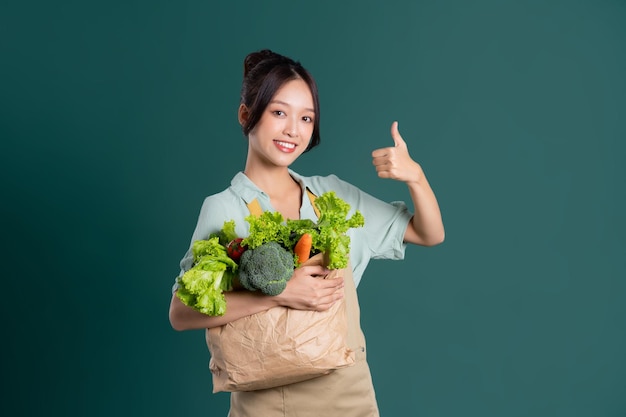 Портрет азиатской девушки с мешком овощей на зеленом фоне