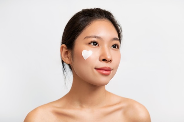 Asian girl posing with heart shaped cream on cheek