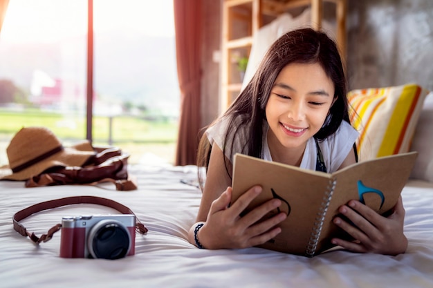 Asian girl read a travel note book on the bed in hone stay