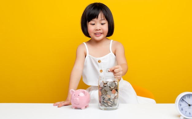 アジアの女の子の手貯金箱にコインを入れる自分の教育のためにお金を節約しているかわいい女の子お金を節約するコンセプト