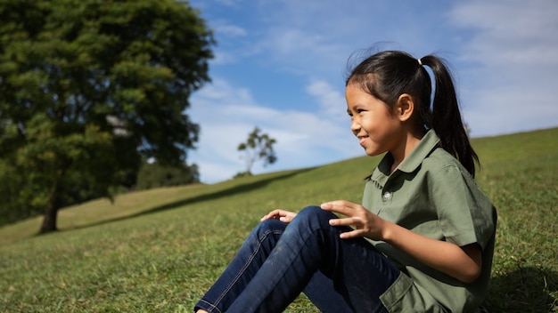 Азиатская девушка сидит на холме с зеленой травой, чтобы наслаждаться красивой природой в летнее время