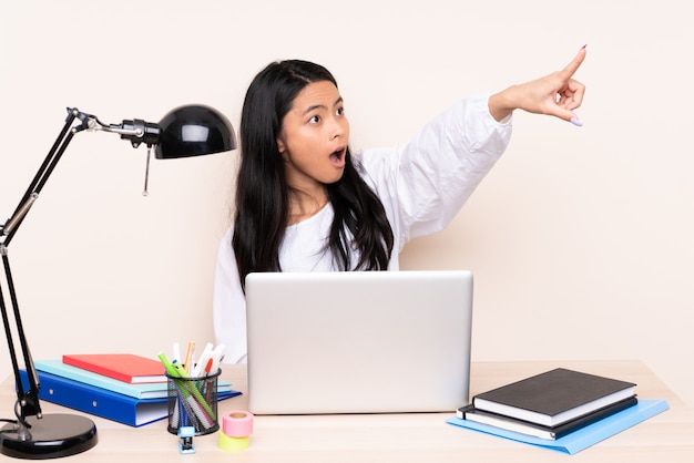 Ragazza asiatica che si siede a un tavolo con laptop e notebook