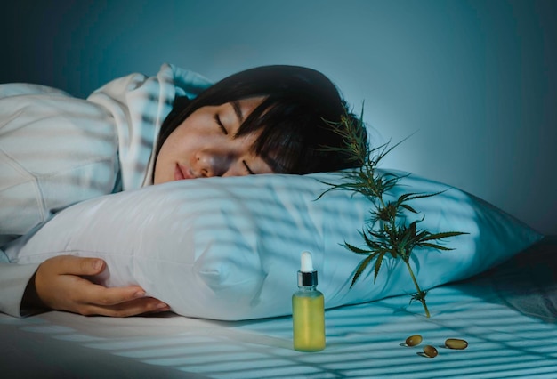 Asian girl sleeping in evening bedroom with cbd oil capsules and a cannabis branch melatonin
