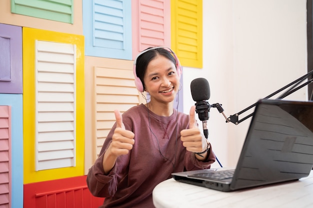 Asian girl smiling in front of microphone while recording video blog with thumbs up