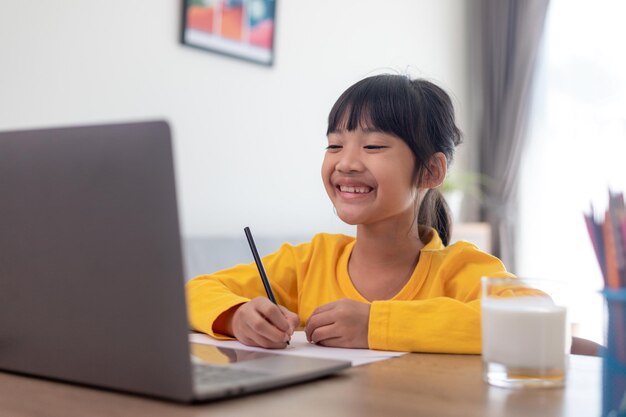 アジアの女子学生オンライン学習クラス学習オンラインビデオ通話ズーム教師、幸せな女の子は自宅でラップトップを使用してオンラインで英語を学びます。ニューノーマル。Covid-19コロナウイルス。社会的距離。家にいる