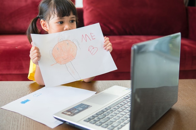 アジアの女子学生のオンライン学習クラスは、自宅のラップトップでオンラインで勉強します。