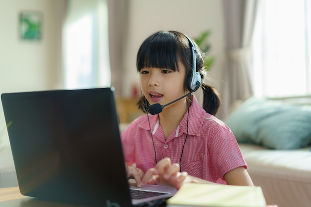 Asian girl student video conference e-learning with teacher and classmates on computer in living room at home.