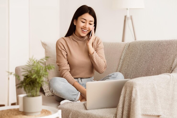 Photo アジアの女の子が電話で話しノートパソコンでインターネットをサーフィンしソファに横たわっています